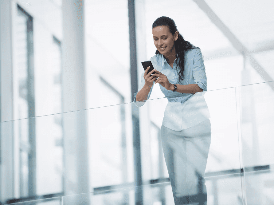 Woman using a smartphone while walking through an office building, representing project coordination and mobile workflow management.