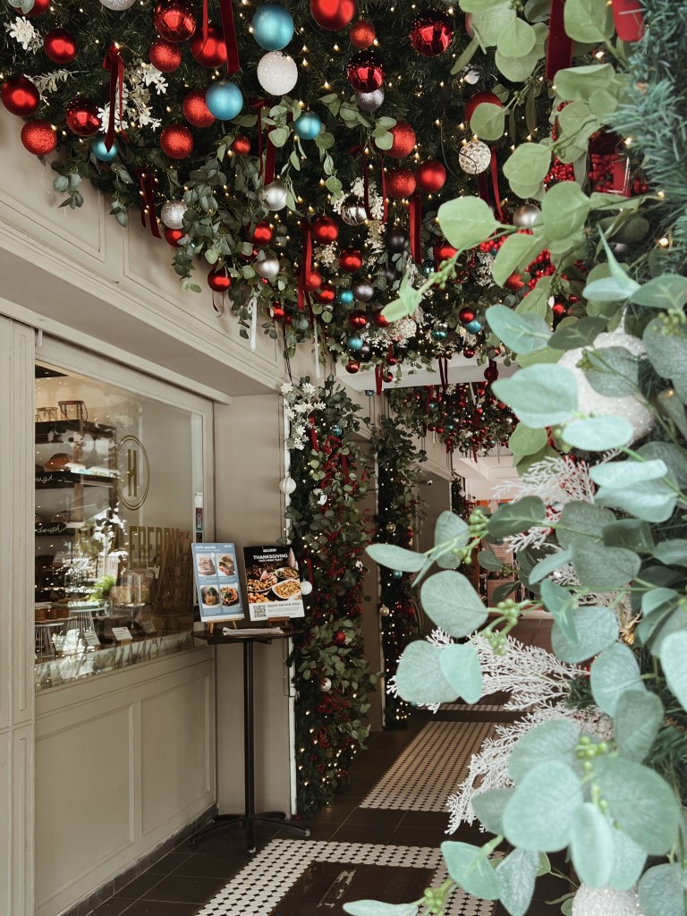 Entrance to Huckleberry decorated for Christmas, featuring festive ornaments in red, silver, and turquoise, with greenery overhead and a menu display at the entrance.