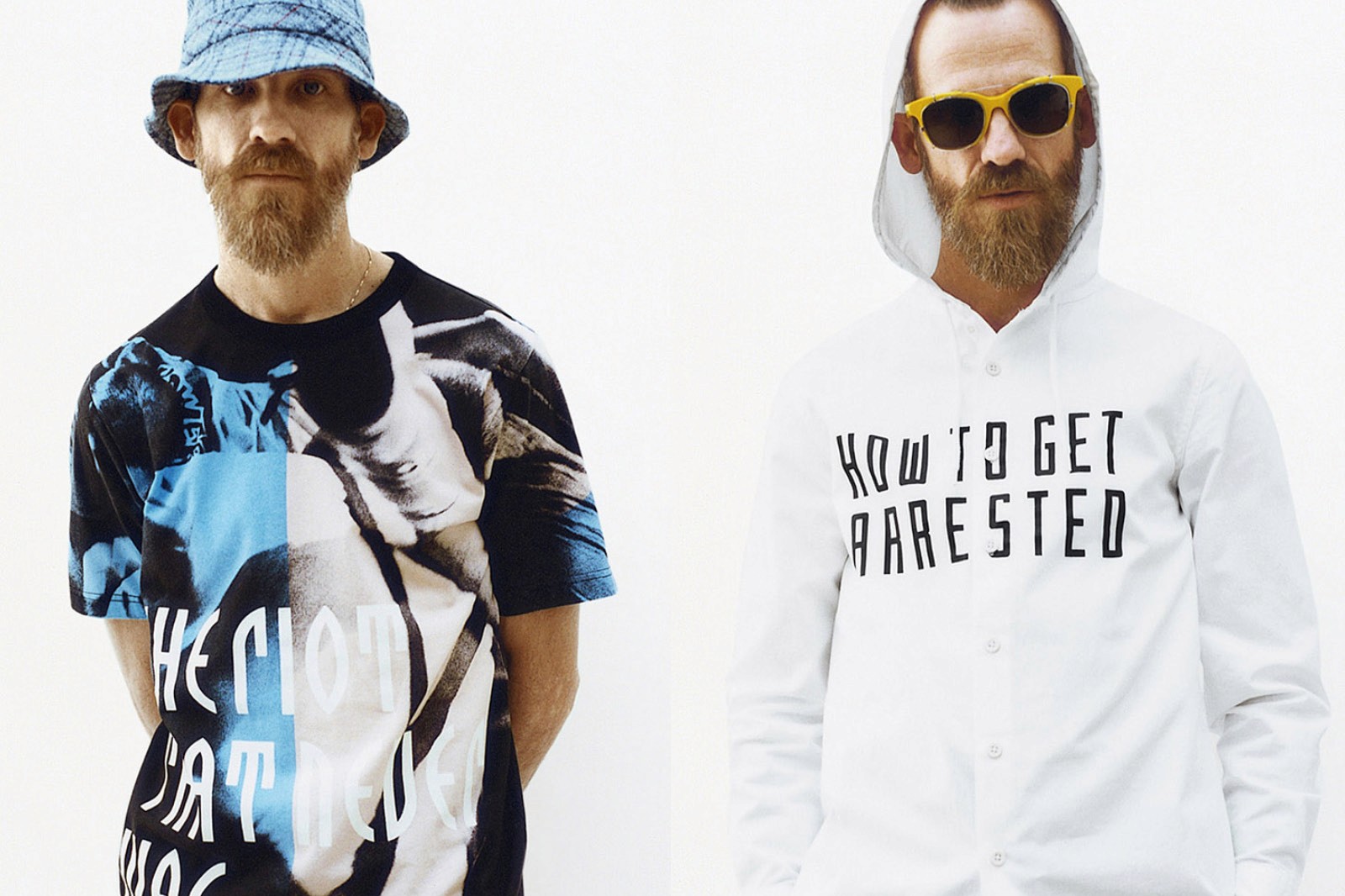 Two men stand side by side, one in a colorful shirt and bucket hat, the other in a white hoodie and sunglasses.