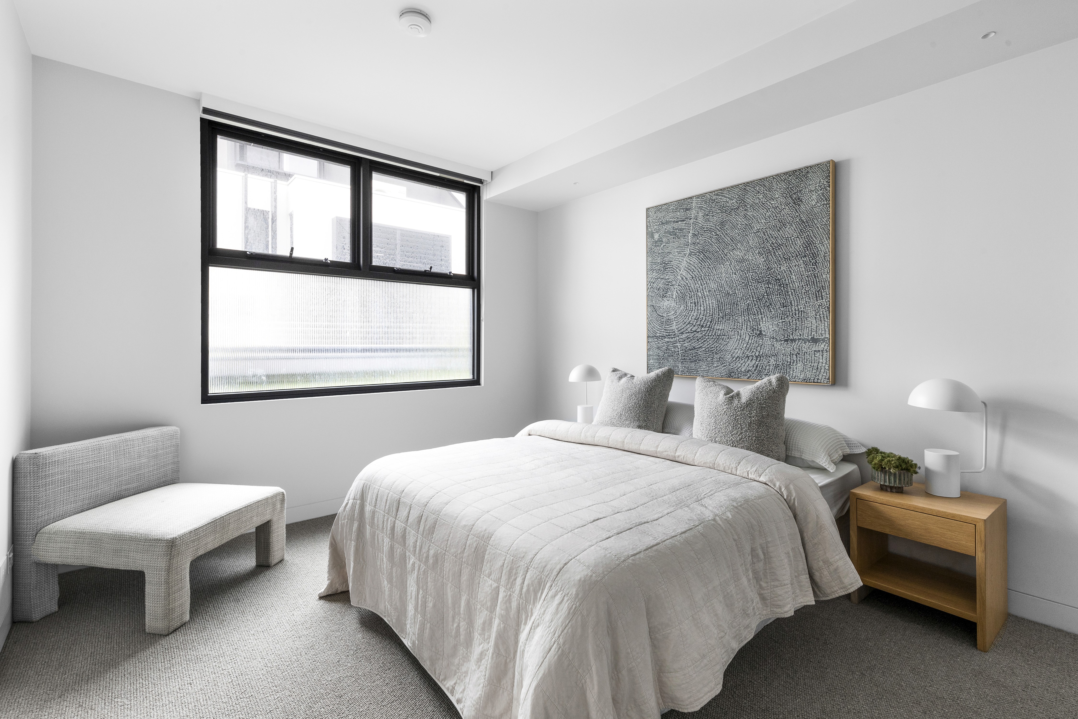 Modern minimalist bedroom with cozy bed, artistic wall décor, and sleek furniture.