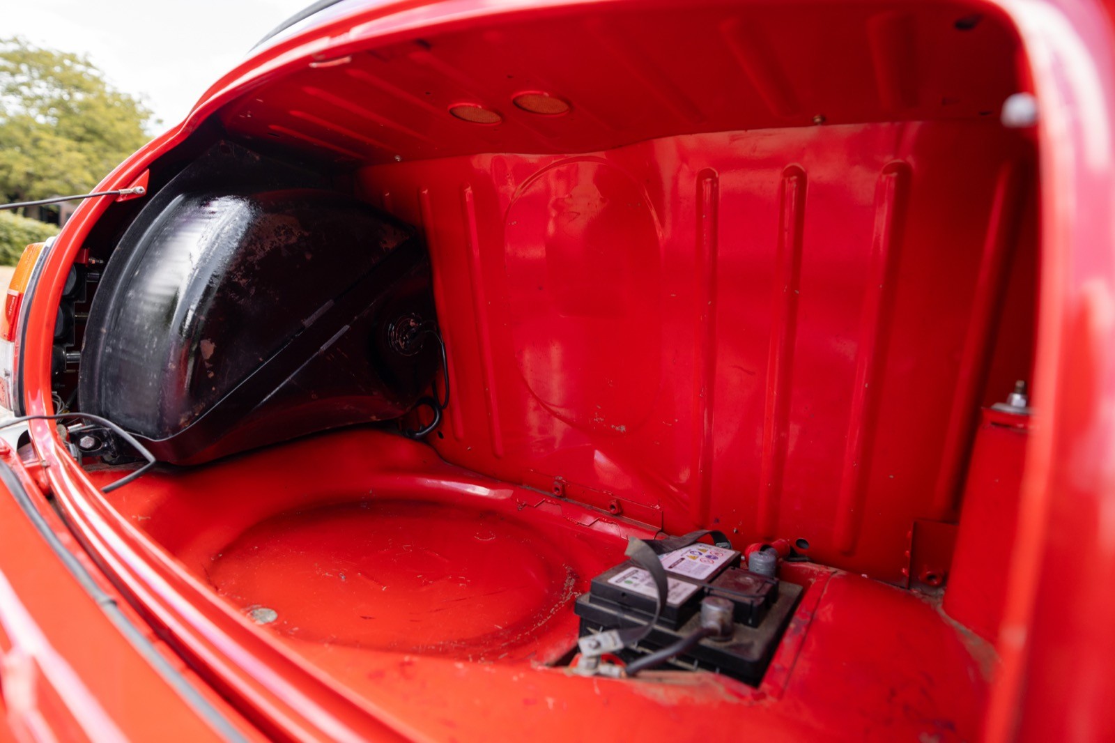 A close-up of a bright red car trunk, featuring a black spare tire and tools in a neat arrangement.