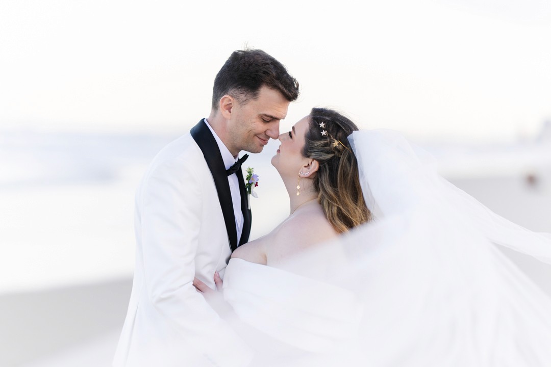 Bride and groom touching noses at beach