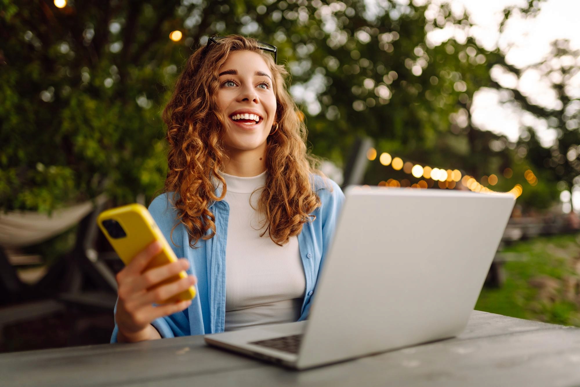 A woman in a striped shirt holds a credit card while using a laptop, bathed in warm sunlight in a cozy, modern setting.