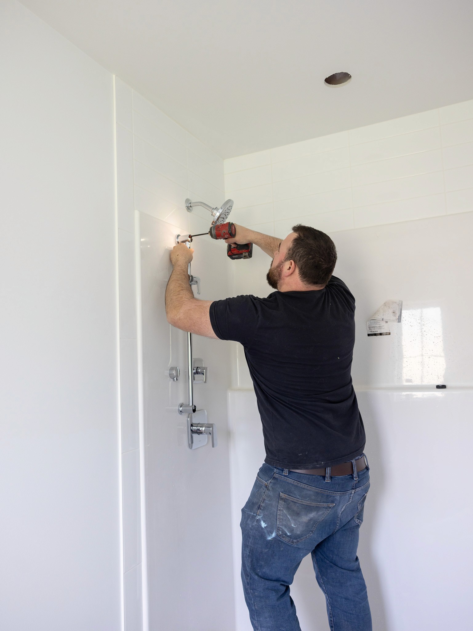 Plumber in Chilliwack, British Columbia, installing shower fixture with drill.