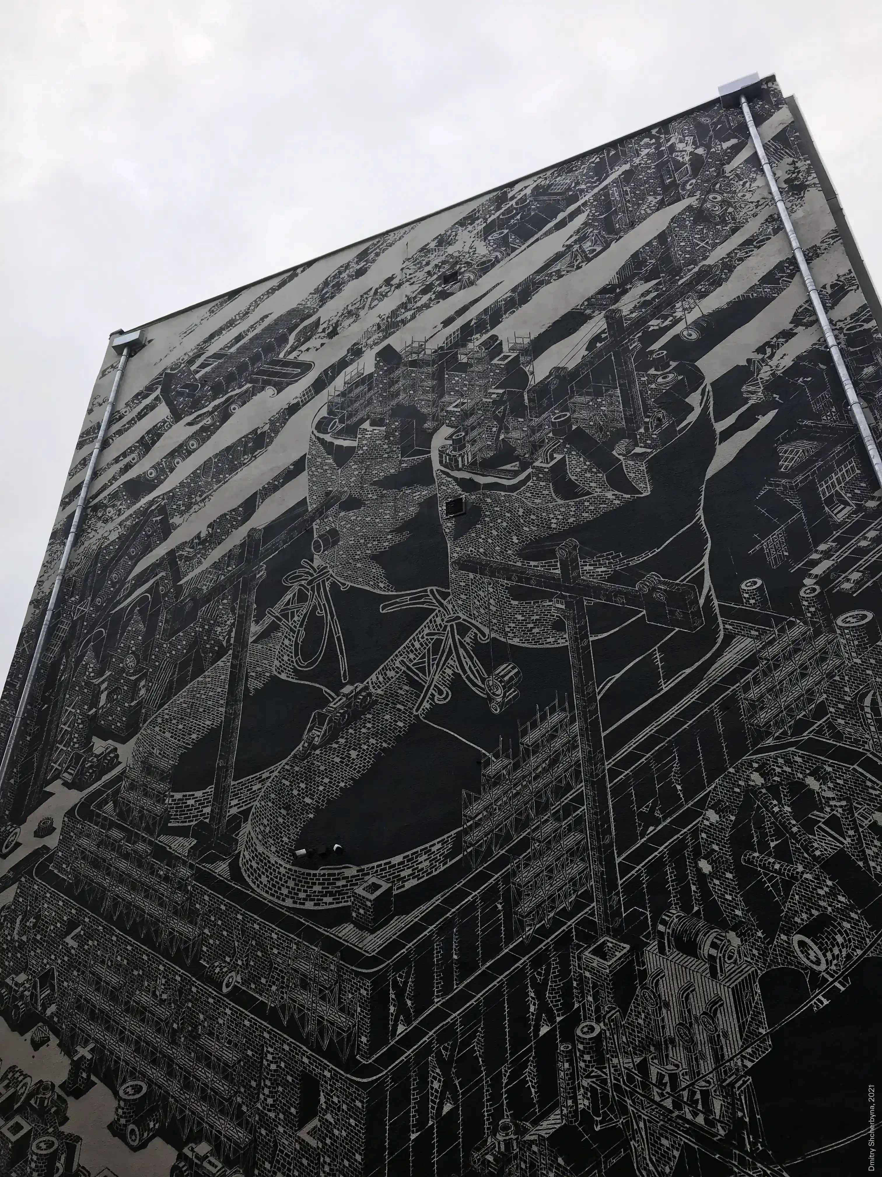 A massive black-and-white mural covers an entire building wall, showing enormous boots. The level of intricacy is reminiscent of etching or engraving.