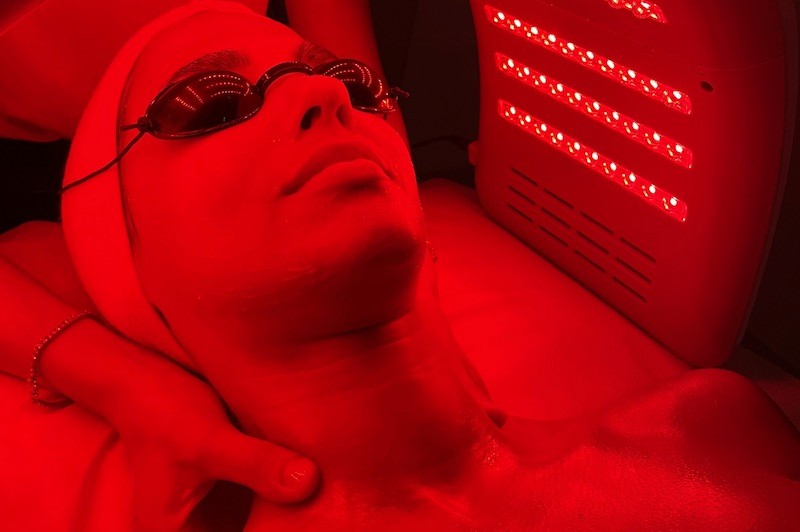 A woman lying down with a towel wrapped around her head, her face glowing with facial oil. She has a peaceful expression, enjoying a skincare treatment.