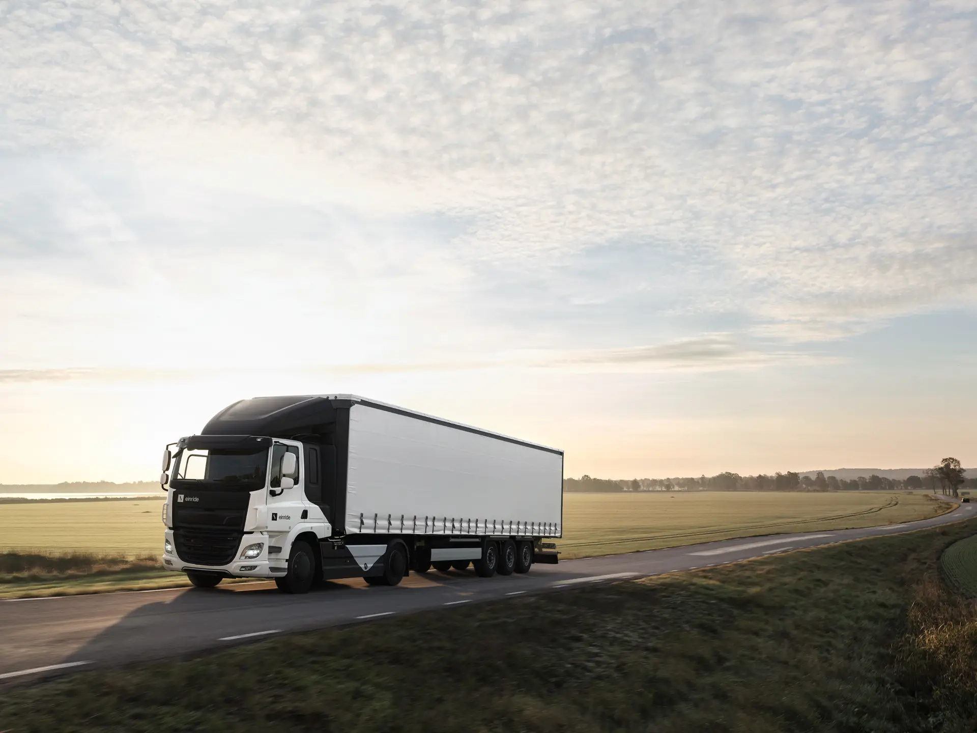 An Einride electric truck driving down a quiet, green country road.