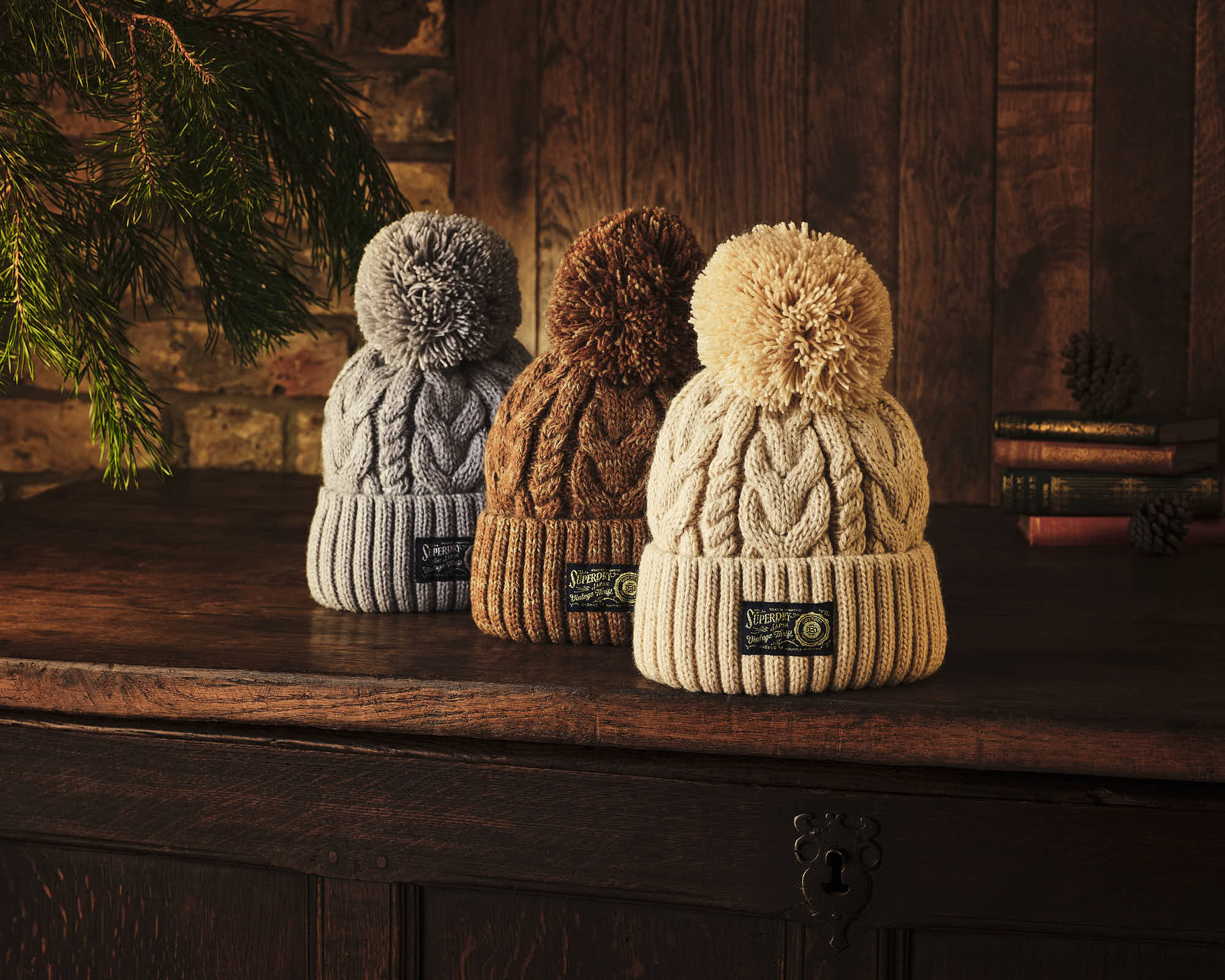 Three small, plush figures in different colors (blue, brown, cream) sit on a wooden surface against a dark background.