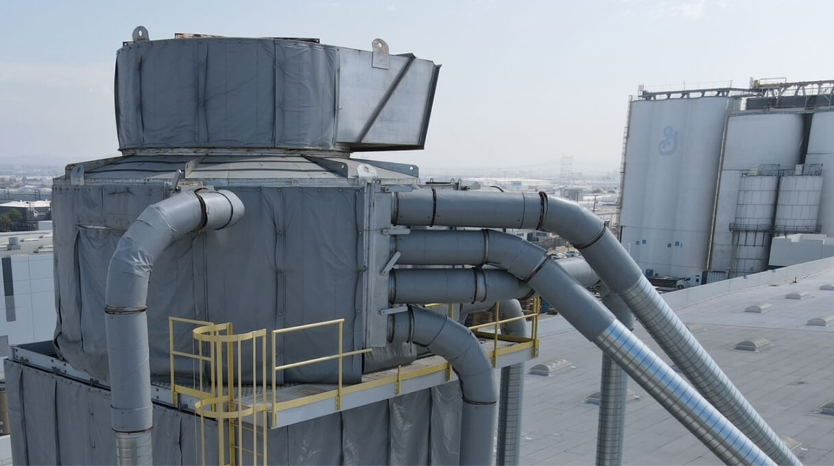 A view of industrial equipment on a rooftop, featuring large gray components and connected pipes.