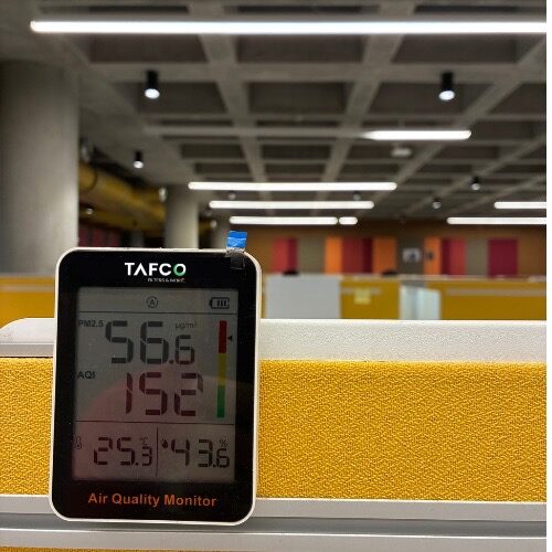 TAFCO air quality monitor showing PM2.5, AQI, temperature, and humidity readings inside a modern open-plan office