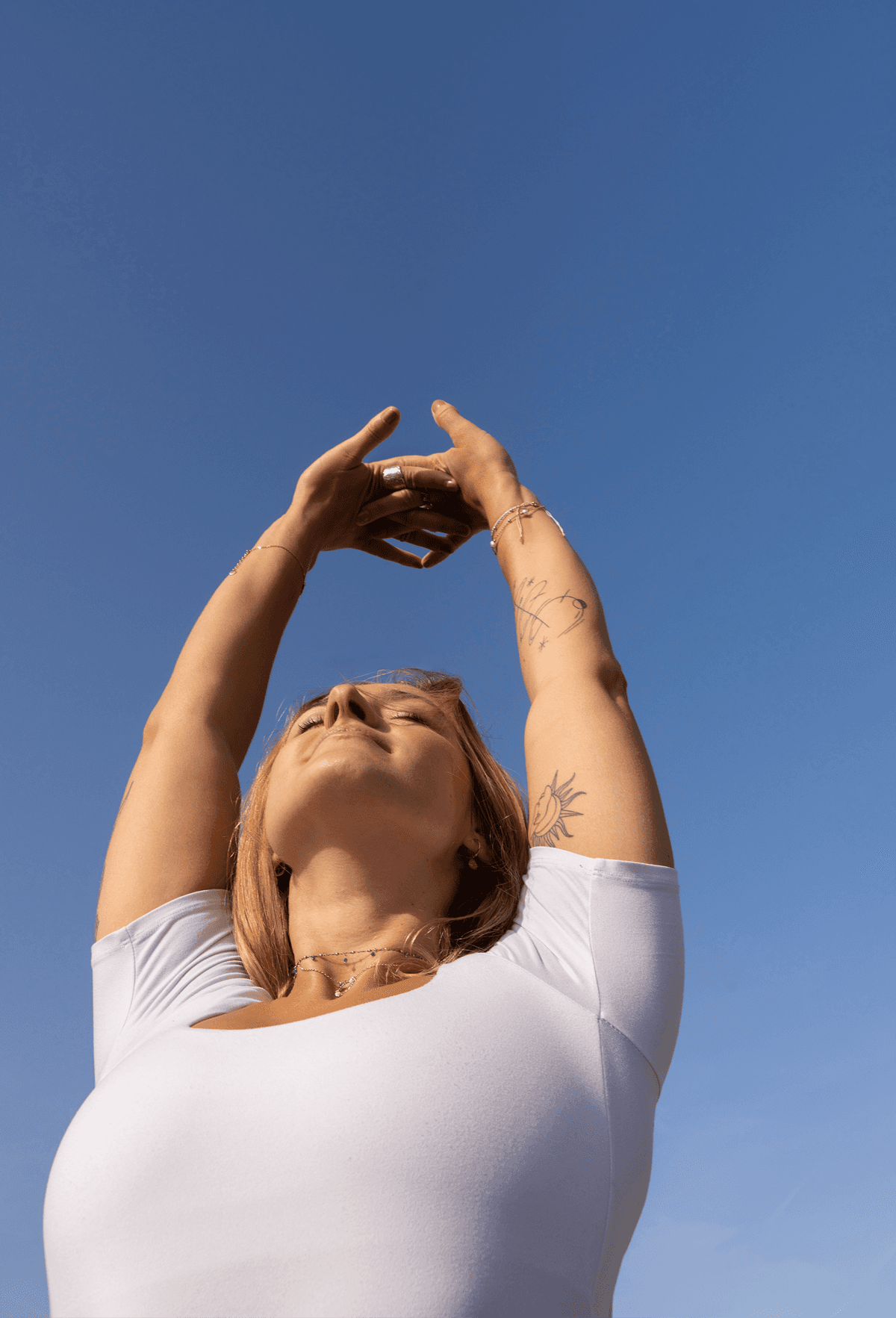 A person is stretching their arms upwards under a clear blue sky, embodying a sense of tranquility and connection with nature, symbolizing a balanced life with yang energy.