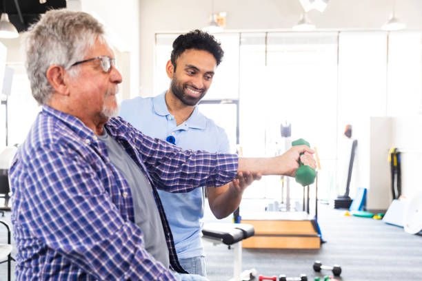 Physical therapist guiding an older man through shoulder strengthening exercises using a dumbbell.