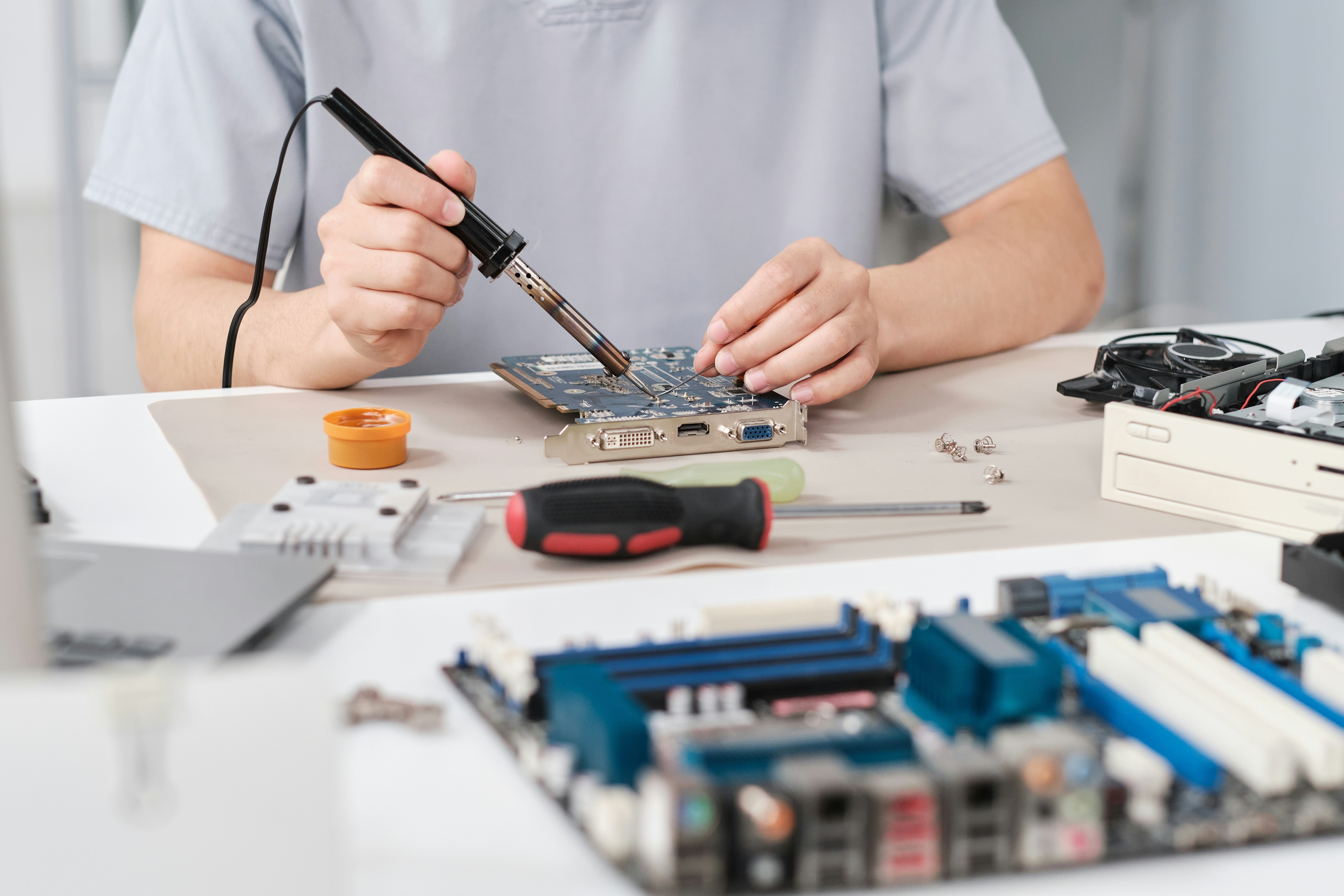 Hands of young repairperson fixing tiny details on motherboard with soldering iron