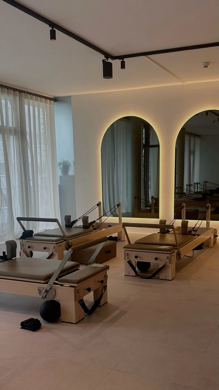 A serene and elegant spa space with wooden reclining chairs and white cushions. Golden sunlight filters through a cascading water feature, creating a peaceful atmosphere. Tropical plants and candles add to the relaxing ambiance.