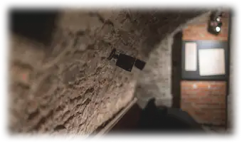 Gros plan sur un mur de pierre voûté équipé de petits haut-parleurs orientés vers une installation immersive.