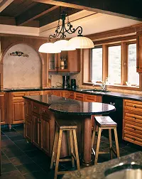Traditional wood kitchen with dark stone countertops, center island, stools, and pendant lighting
