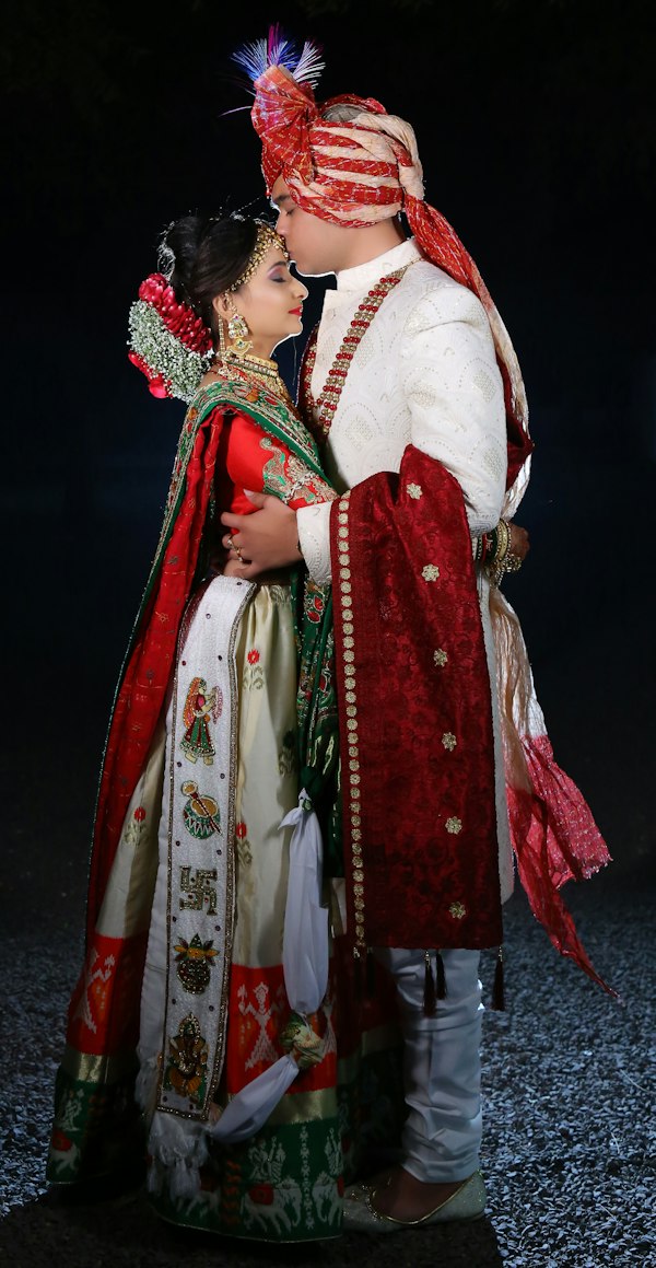 Groom in a white sherwani kissing the bride’s forehead
