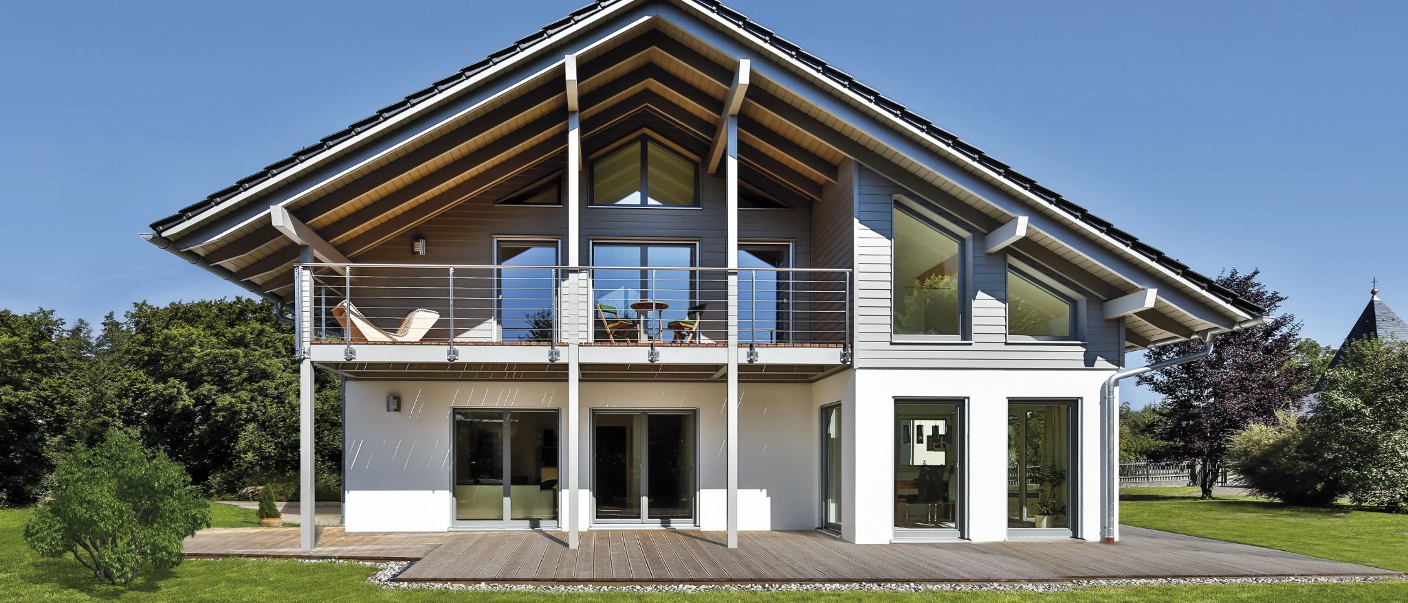 Modernes Einfamilienhaus mit großem Balkon, Glasfronten und einem Dachüberstand aus Holz.