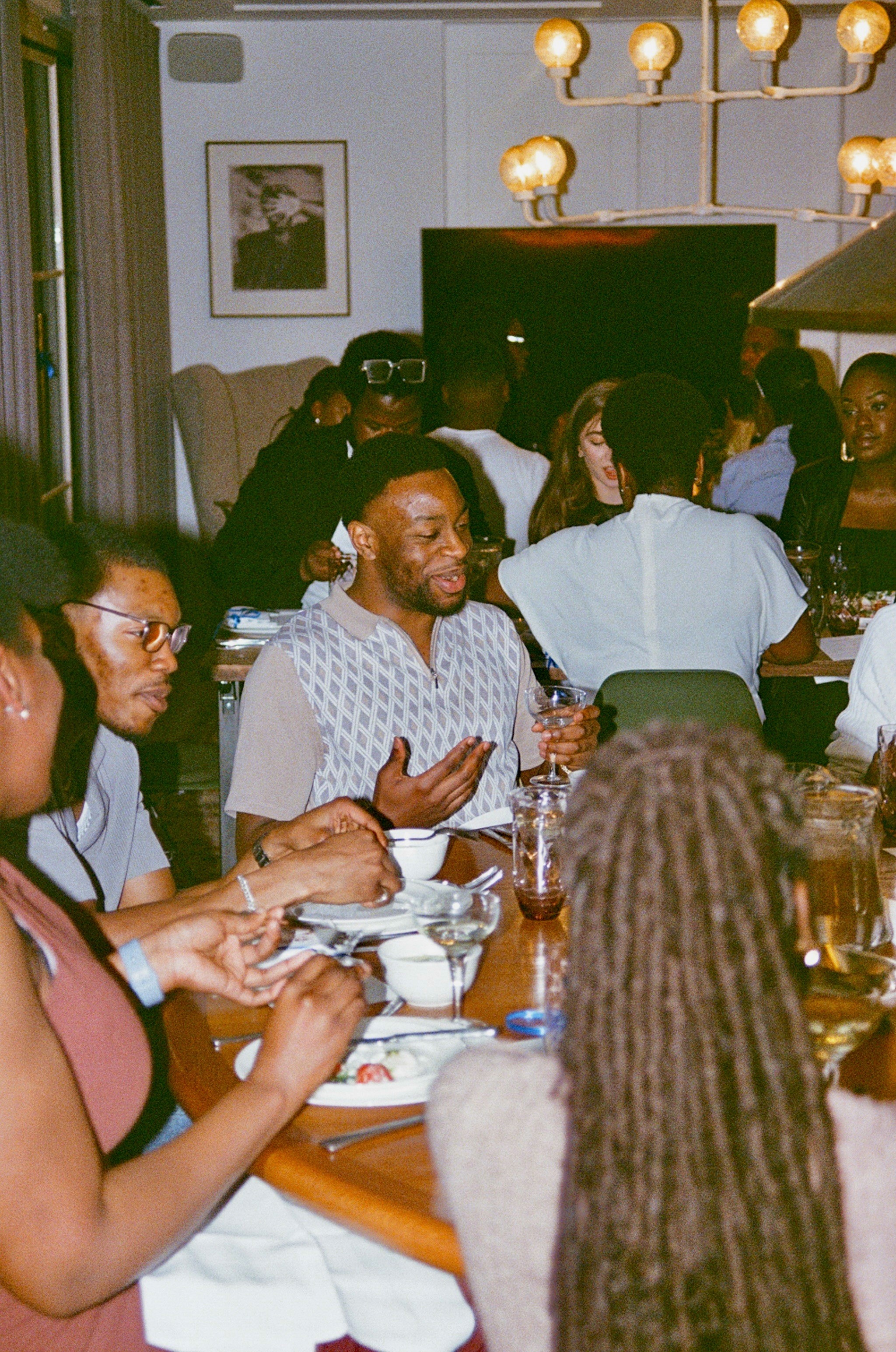 Group of diverse friends enjoying a meal together at a restaurant, with one man in the foreground talking and gesturing.