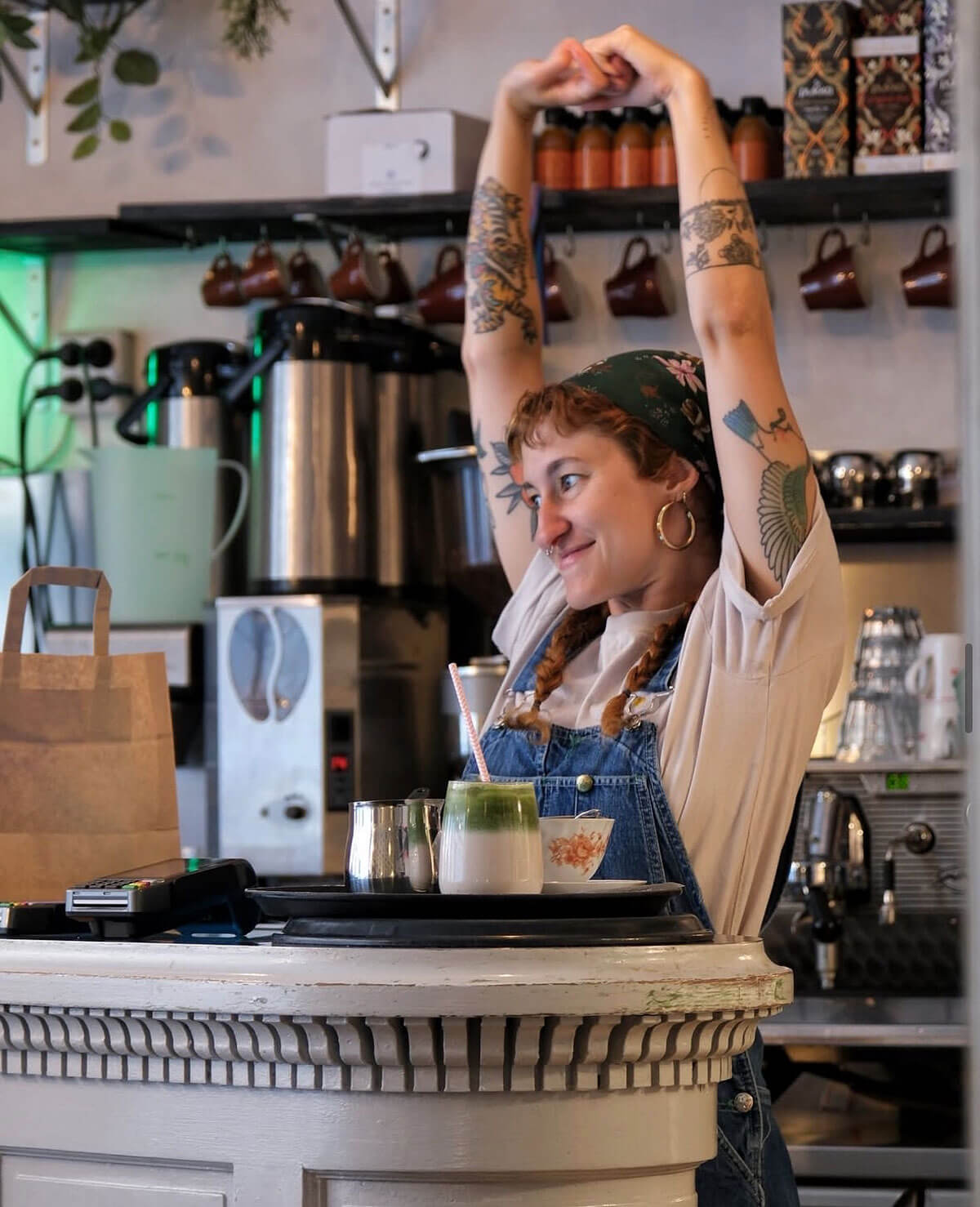 Barista standing behind the bar with her arms in the air and smiling.