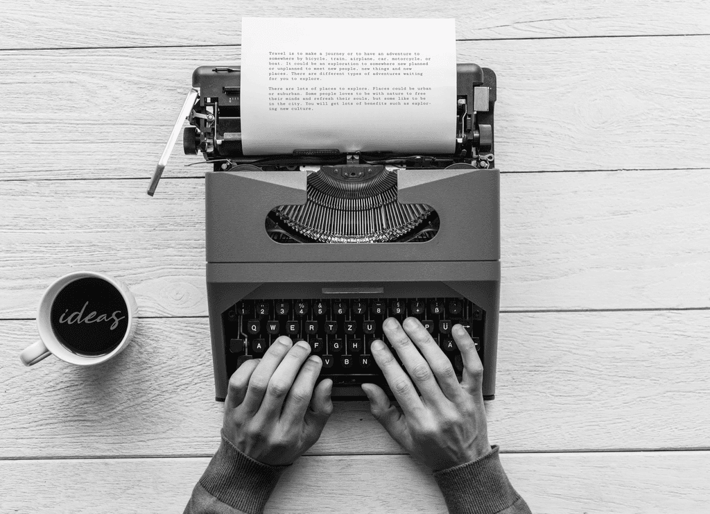 person writing on brown wooden table near white ceramic mug