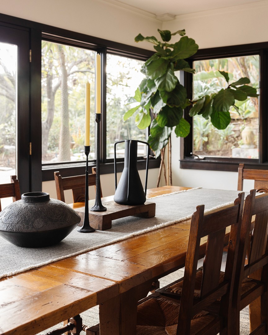 This tranquil gathering spot features earthy tones, a wooden overhead structure, and a stone fire-pit, complemented by wicker accents and sectional seating for a cozy, shaded escape