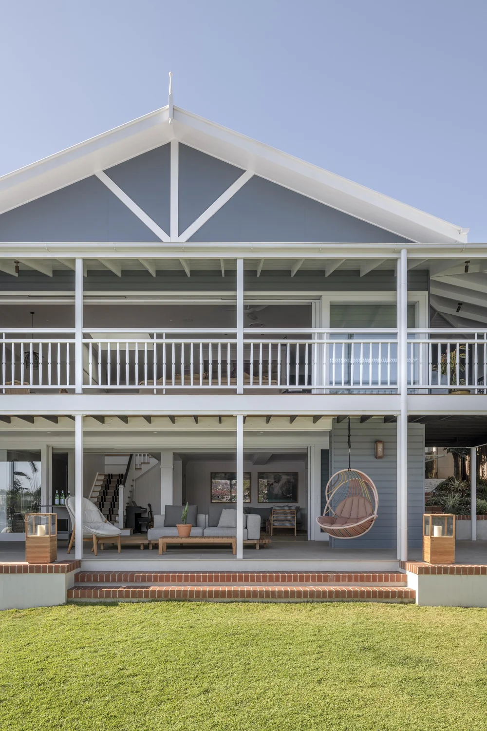 Rear view of a two-storey home with gabled roof, wraparound balcony, and open indoor-outdoor living area.