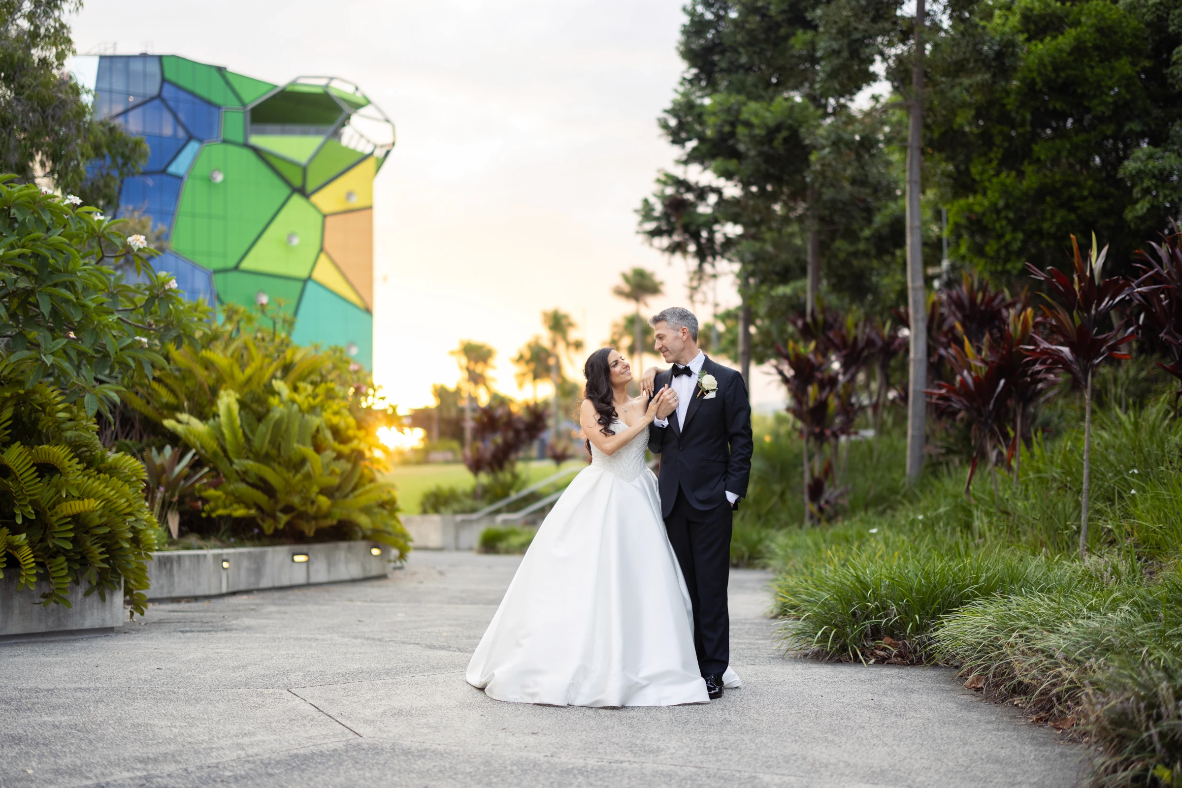 Bride and groom looking into each other's eyes walking through a garden at sunset