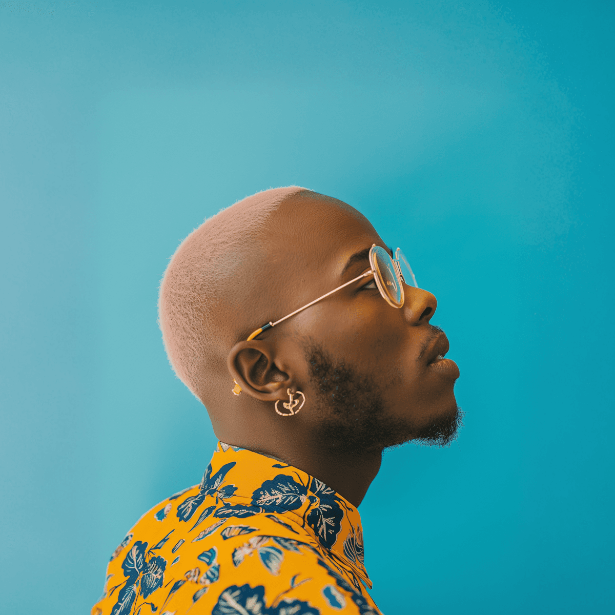 Stylish person with pastel pink hair wearing round sunglasses and a yellow floral shirt, posing in profile against a bright turquoise background.