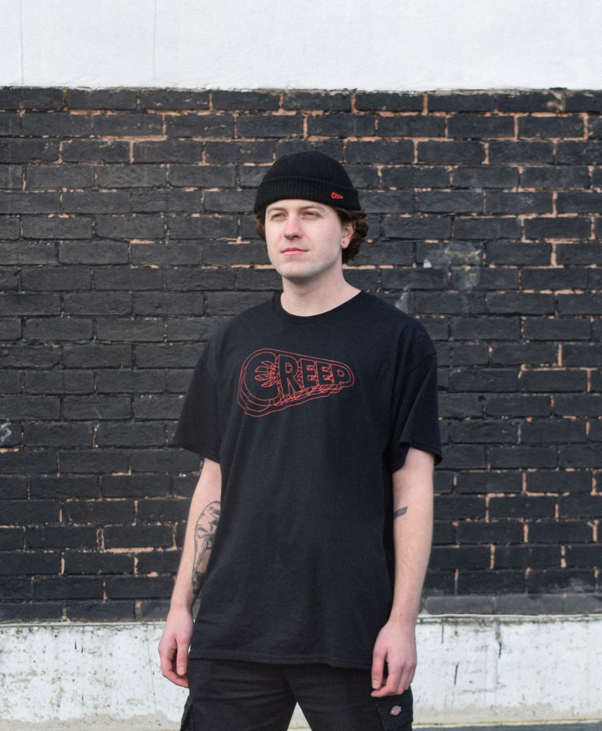 model wearing black creep hologram t-shirt against black brick wall.