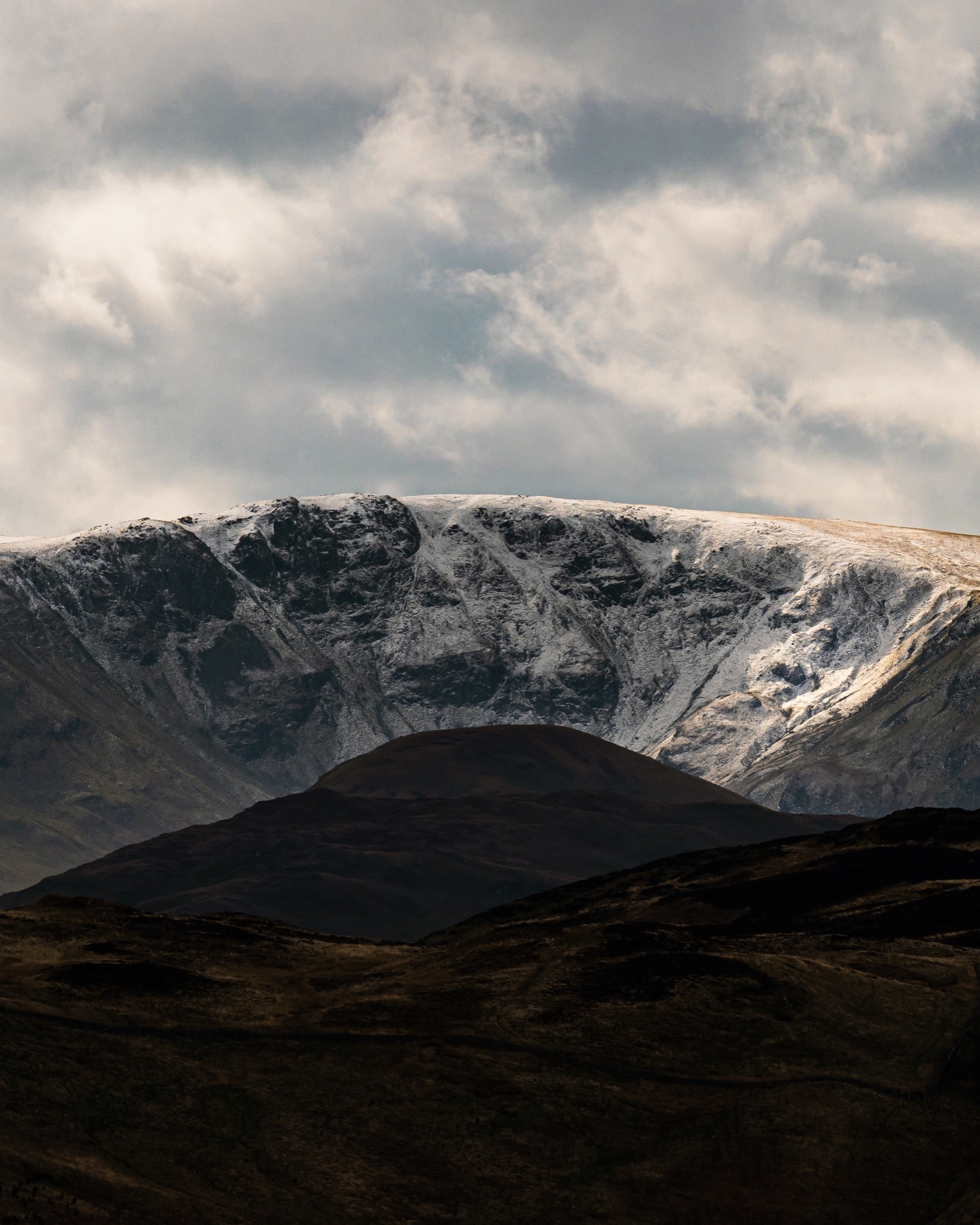 Kidsty pike in a dark moody scene with snow. A small mountain called the Nab creates a silhouette in front.