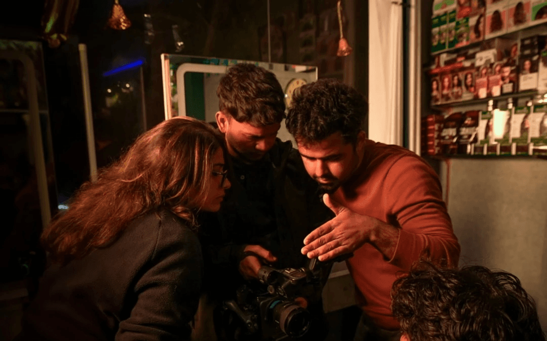 Side view of a woman in a red sweater and white trousers in front of a large red square on a blue wall.