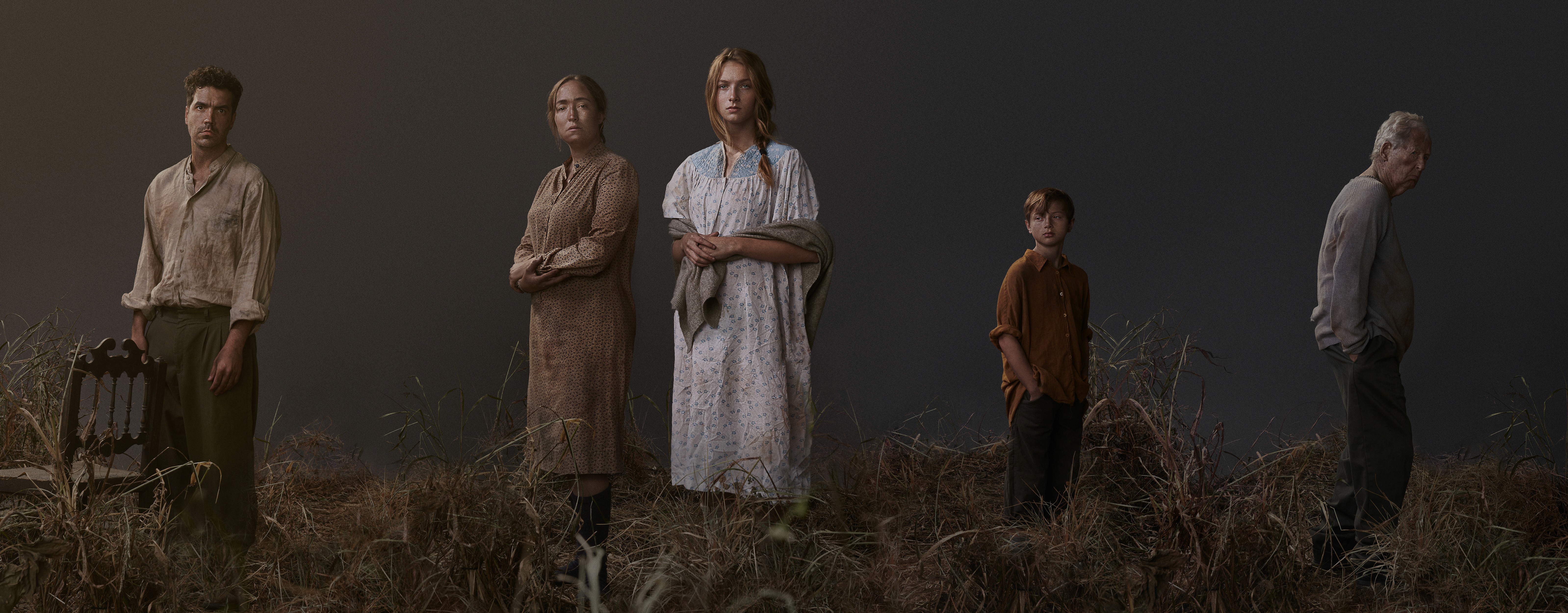 A moody and tense cast photo of 19th century characters stood in grassland.  The image is in the style of TV show publicity key art. 
