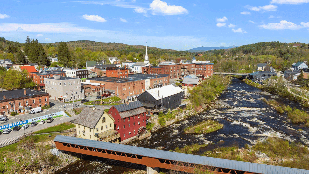 Aerial view of downtown Littleton, NH with covered bridge, Ammonoosuc River, and White Mountains in the background — short-term rental regulations vary by town across New Hampshire