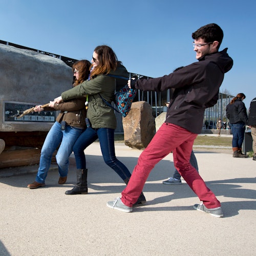 Three people smiling and pulling a rope together in an outdoor setting on a sunny day.