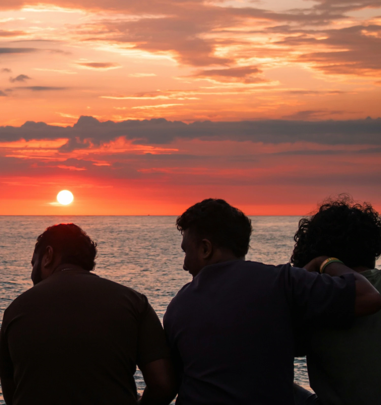 Silhouette of four friends sitting together watching the sunset over the ocean, representing community, chosen family, and LGBTQ+ family therapy support in New York City.