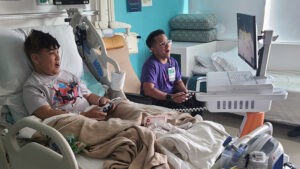 A patient and gaming tech specialist compete in NBA 2k on a GO Kart in a hospital room.