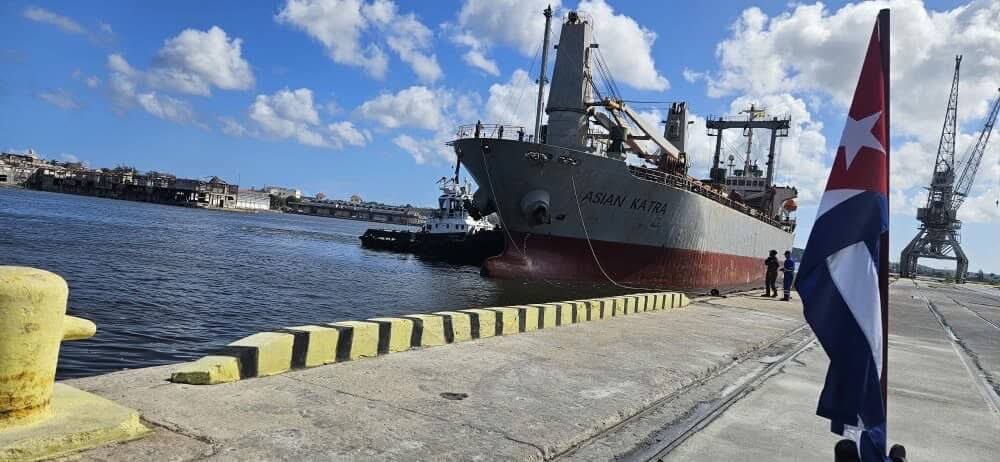 Cargo ship docked at a Cuban port with a Cuban flag in the foreground.
