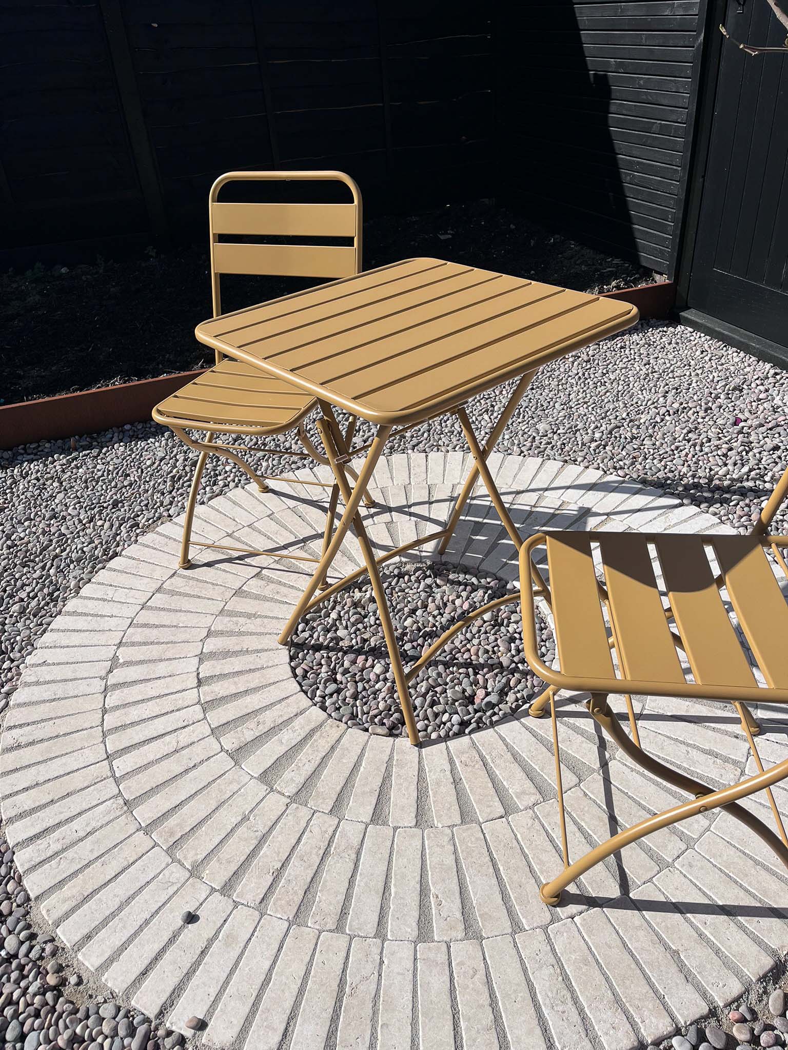 A small wooden table with two chairs is set on a circular patterned surface, against a dark background.