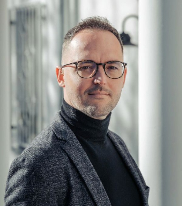 Junger Mann mit Brille, frontal über die Schulter in die Kamera lächelnd.