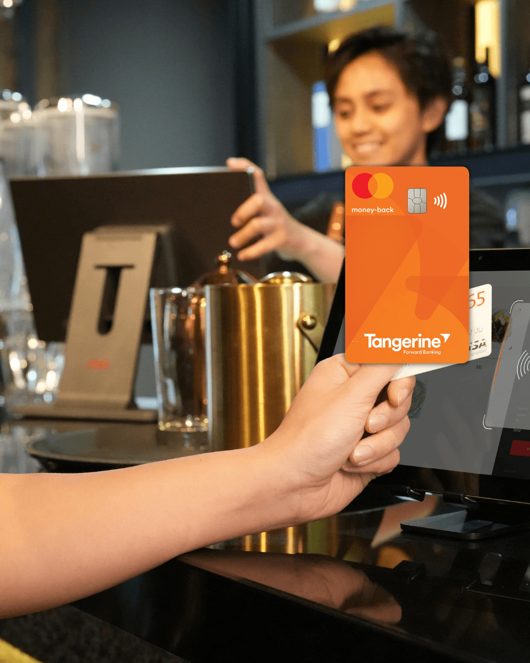 Person tapping their Tangerine Money-Back Mastercard at a payment terminal to earn cash back on everyday purchases in Canada.