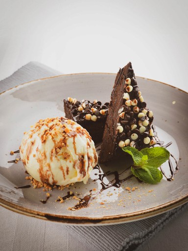 Two slices of chocolate brownie with white chocolate chips served with a scoop of vanilla ice cream, drizzled with sauce and garnished with mint.