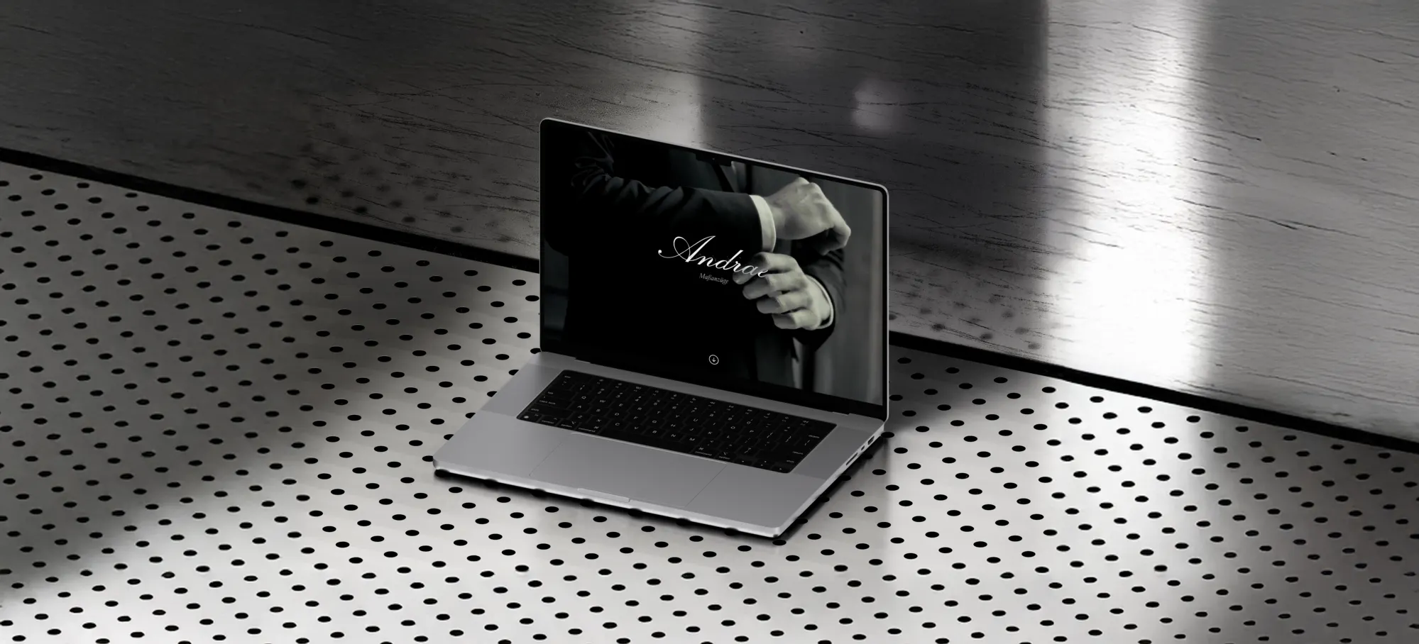 Ein Bild von einem Macbook welches die Hero Section von Andrae Maßanzüge zeigt. Das Macbook steht auf einem Metalboden mt Löchern.