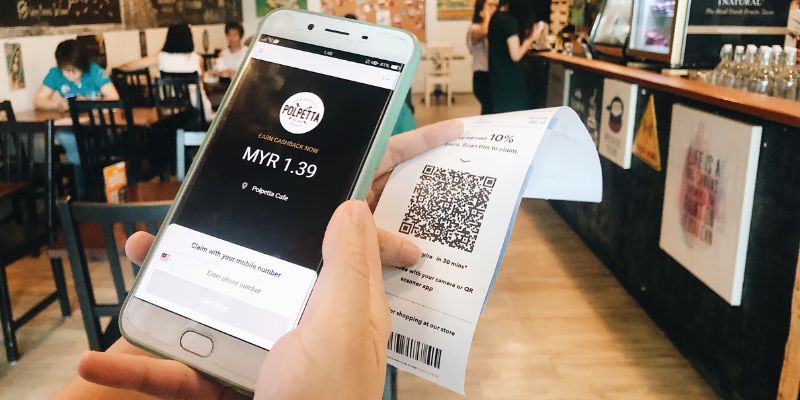 Seorang pelanggan mengimbas resit untuk Cashback menggunakan telefonnya di sebuah kafe.