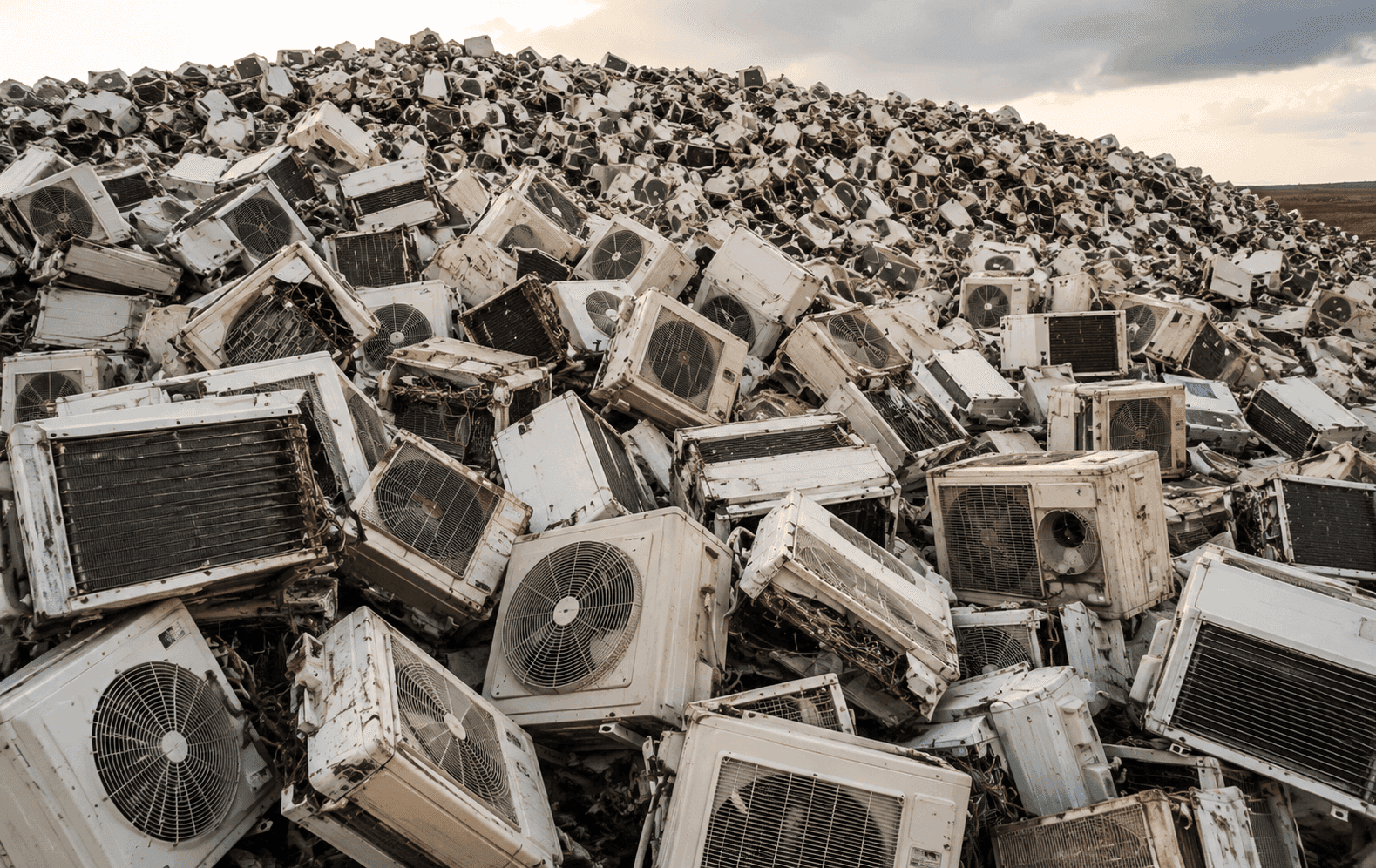 Pile of discarded white air conditioning units, outdoor condenser units, and ventilation equipment in a landfill.