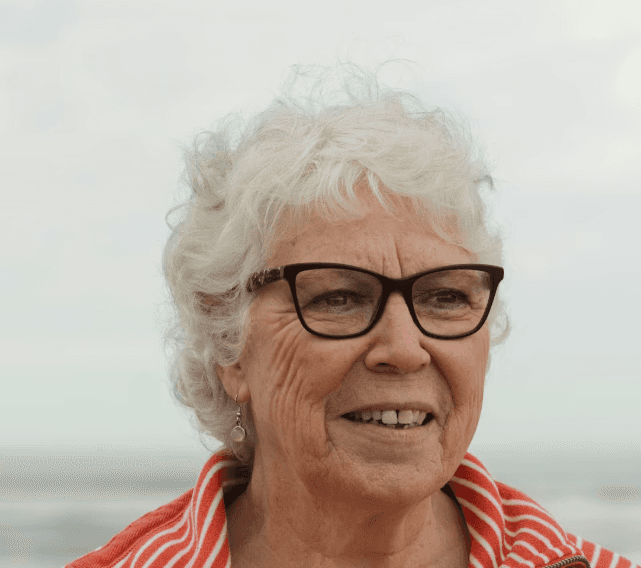 a young man wearing glasses standing in front of a mountain