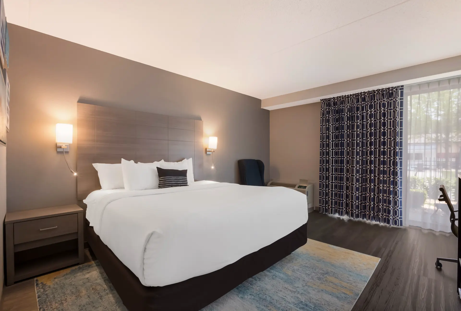 Modern hotel room with a bed, desk, and sofa.