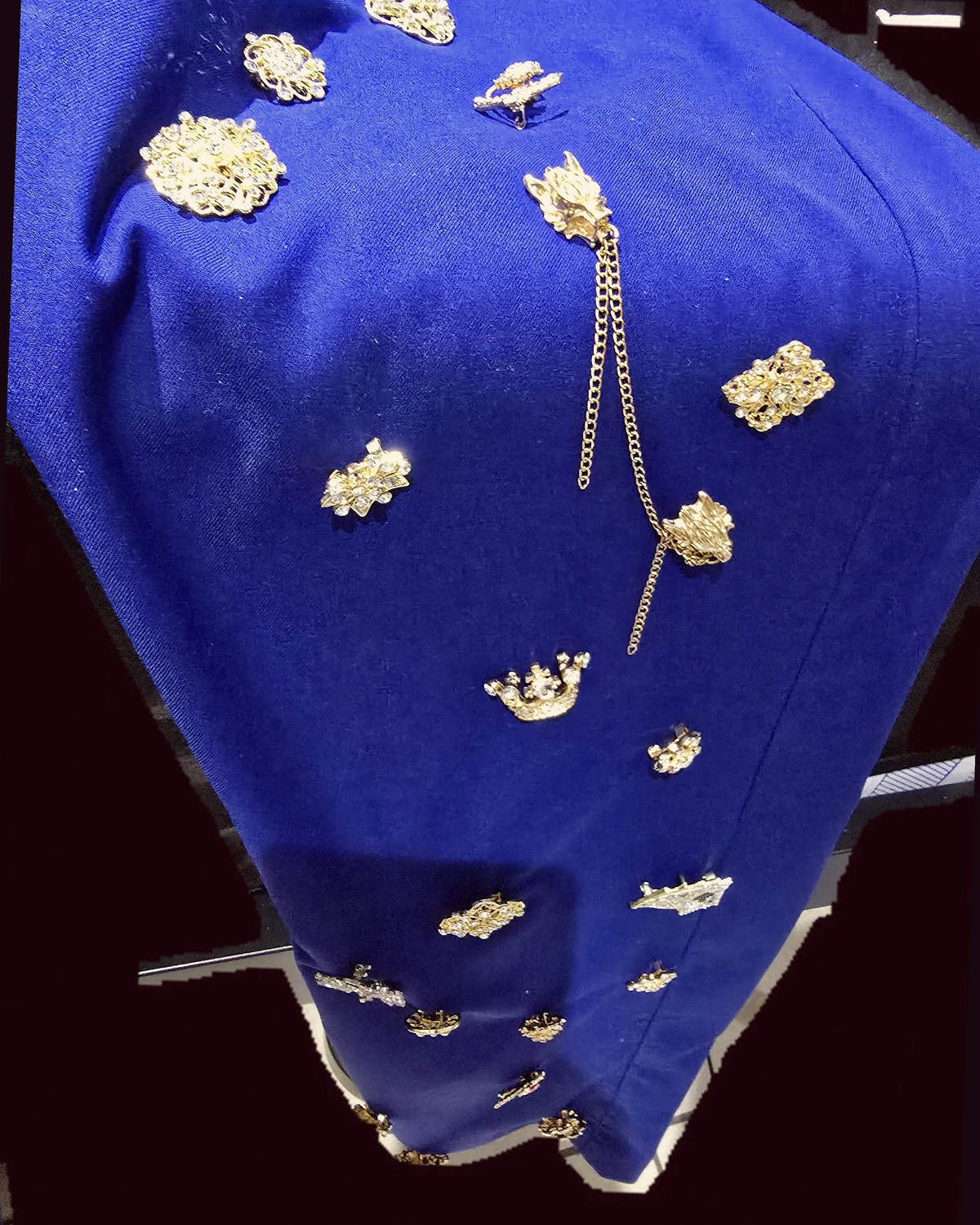 Close crop of one Wonder Suit trouser leg with the original gold brooches under a warm pink filter.
