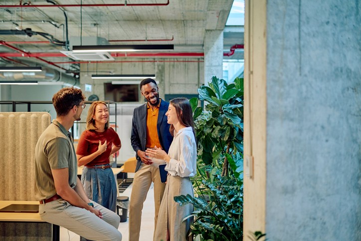 woman is speaking to a group of happy coworkers standing around her