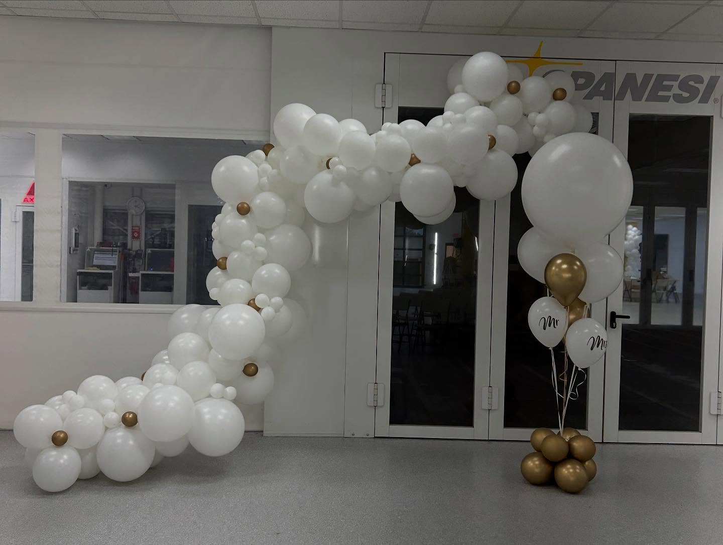 Elegant white balloon garland with gold accents framing a doorway or event entrance created by Be Bold Balloons